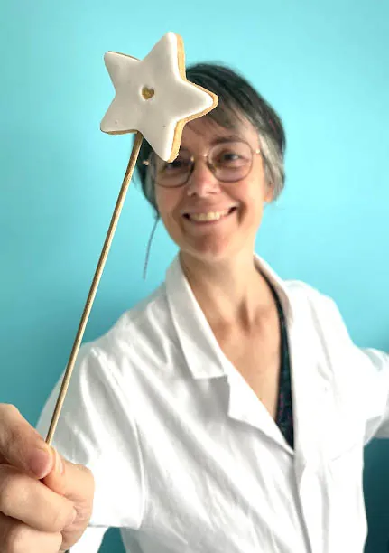 Mélanie, la créatrice de La Fabrique de Méline, souriante en blouse blanche, tient une baguette ornée d’une étoile en biscuit