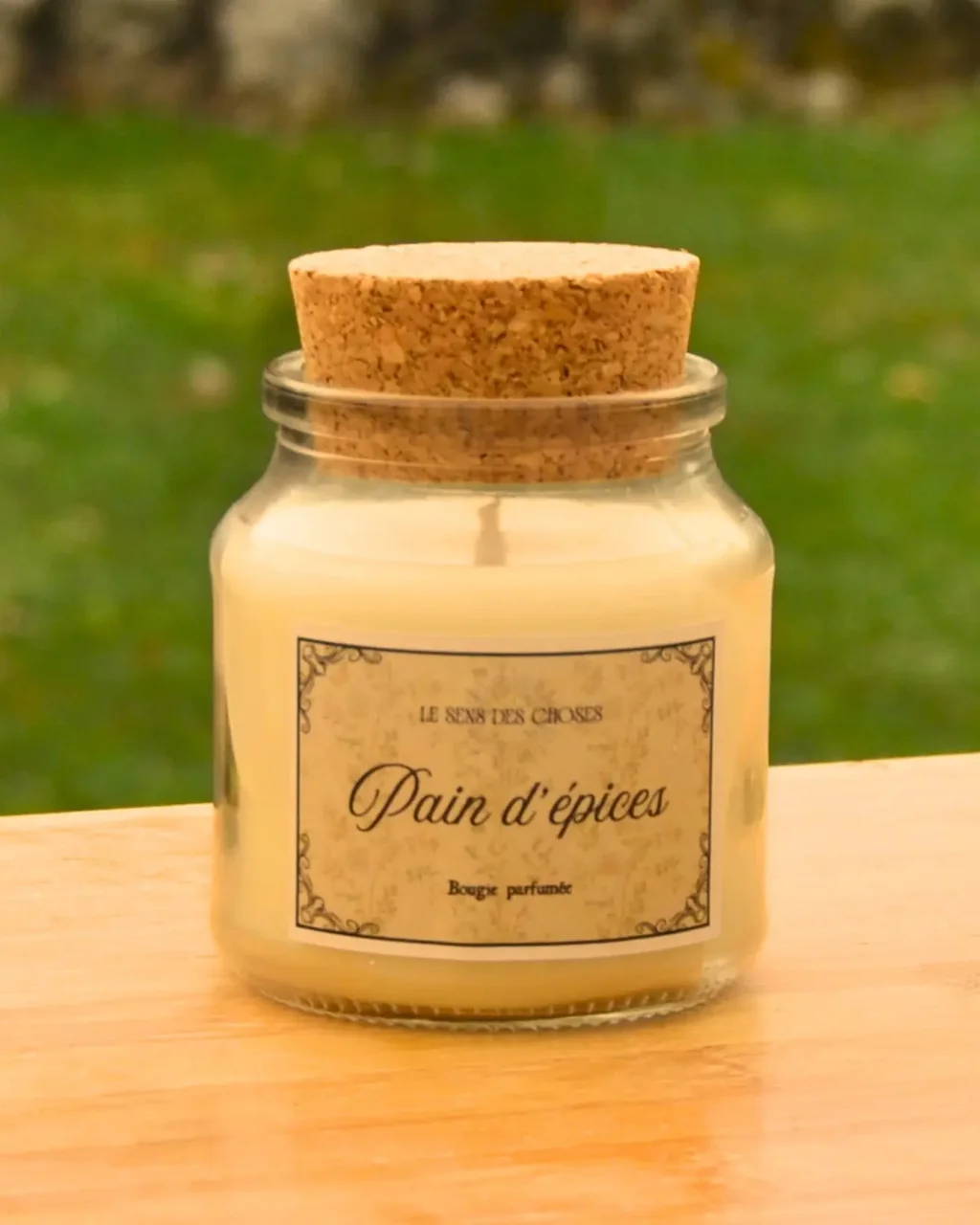 Une bougie végétale « Pain d’épices » dans un pot en verre fermé d’un bouchon de liège, posée sur une table en bois au soleil