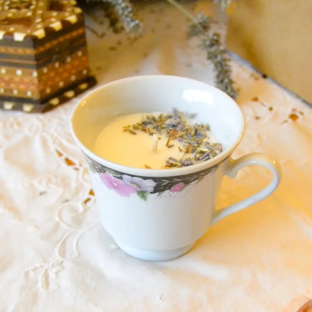 Une bougie végétale coulée dans une tasse ancienne en porcelaine à fleurs, parsemée de boutons de lavande séchée