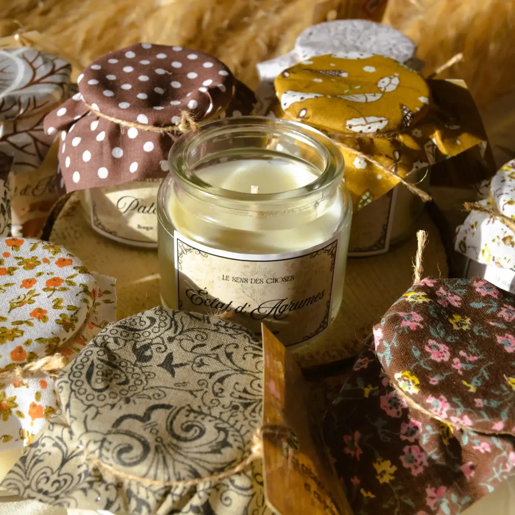 De petites bougies en pots de verre coiffés de tissus à motifs fleuris et à pois, noués d’un cordon