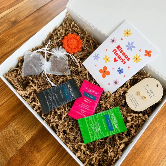Open witte cadeaubox met drie Fauchon-theezakjes, een zakje Bisous Fleuris-bloemzaden, oorbellen, bloemvormige zeep en twee kleine organzazakjes